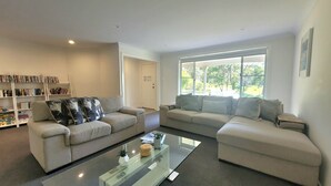 En moderne stue med to sofaer, et glasbord og en reol fyldt med bøger.