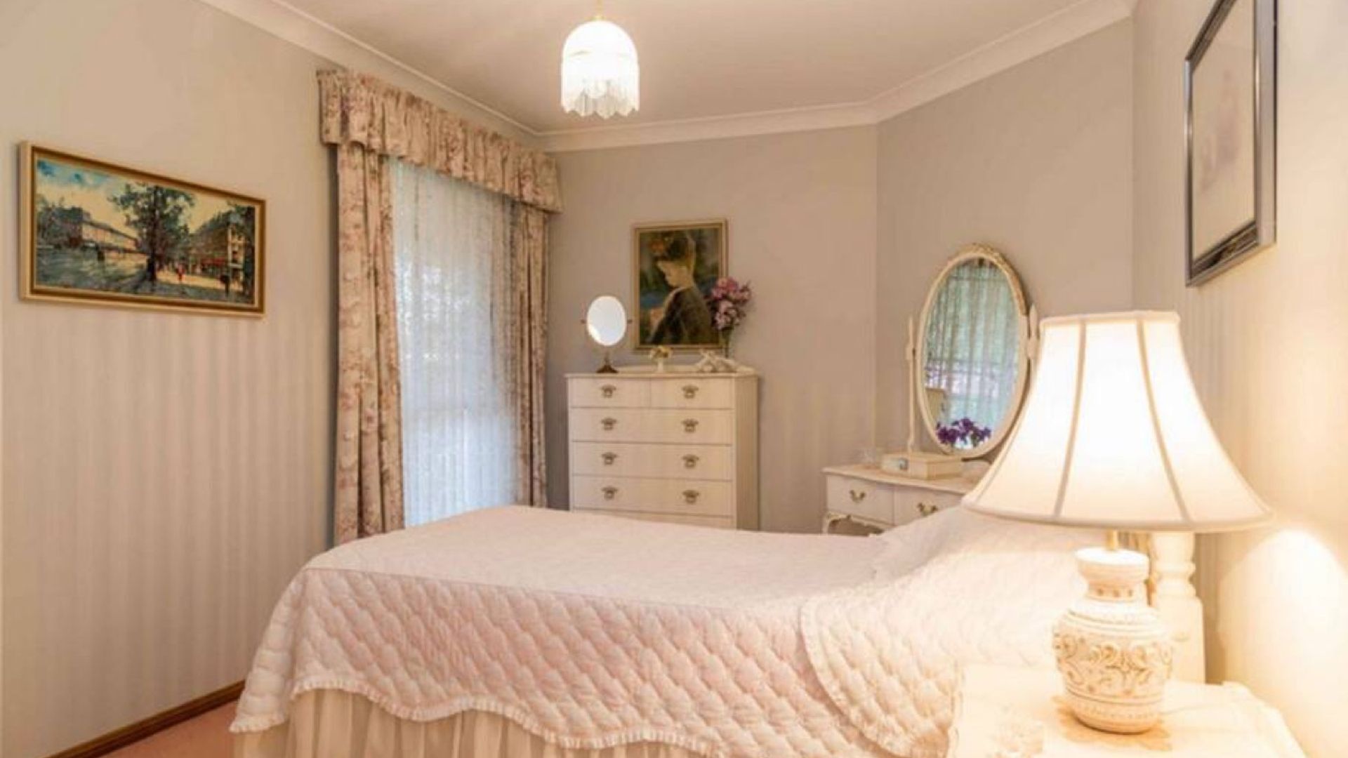 A bedroom with a bed, a dresser, a mirror, a lamp, and a painting on the wall.