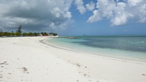 A beach with white sand, clear turquoise water, and a few scattered clouds in the sky.