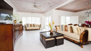 A spacious living area with a wooden ceiling, a sofa set, a coffee table, and a TV mounted on the wall.