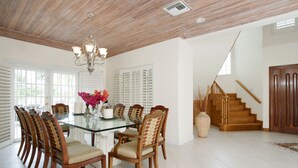 A dining area with a glass table surrounded by wooden chairs, a chandelier, and a vase with flowers.