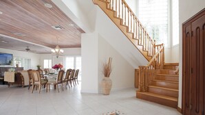 A spacious living area with a wooden staircase, a dining area with chairs and a table, and a large vase with dried plants.