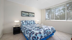 Un dormitorio con cama, dos lámparas de noche, una ventana con persianas y un cuadro en la pared.
