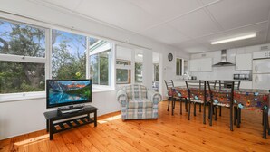 Una sala de estar moderna con televisor, un comedor con mesa y sillas, y una cocina con armarios blancos.
