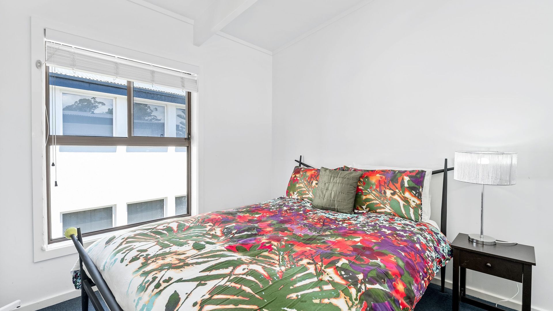 A bedroom with a bed, a nightstand, a lamp, and a window with blinds.