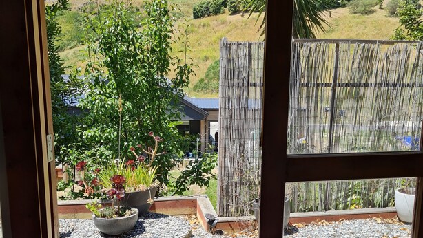 A view from a room's door to an outdoor area with a wooden deck, a welcome mat, and a garden with plants and a bamboo fence. - Quiet self-contained 3 km from Nelson CBD  (Atawhai)