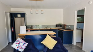 A modern kitchen with a central island, blue cabinets, and a microwave. There are two dark blue chairs with colorful cushions. - Quiet self-contained 3 km from Nelson CBD  (Atawhai)