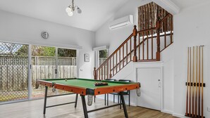 A billiards table in a room with a wooden floor, a staircase, and a view of the outside.