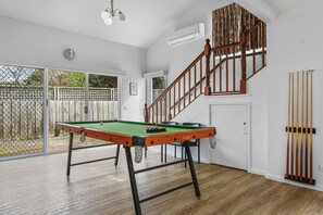 A billiards table in a room with a wooden floor, a staircase, and a view of the outside.