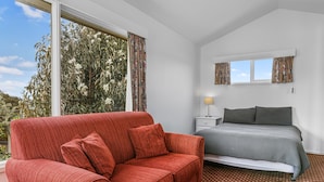 A bedroom with a red sofa, a bed with a patterned bedspread, a nightstand with a lamp, and a window with curtains.