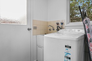 A laundry area with a washing machine, a sink, and a window. - Aunty Wins (Apollo Bay)