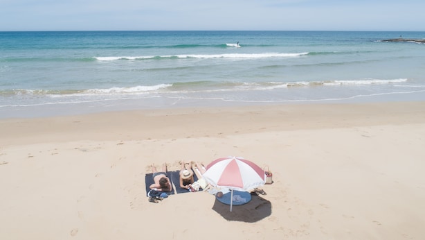 A beach with a sandy shore, a person lying on a towel, and a beach umbrella.