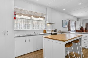 A modern kitchen with white cabinetry, a wooden island, and a large window with lace curtains.