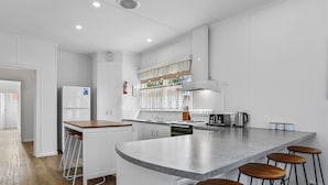 A modern kitchen with white cabinetry, a large island with stools, a built-in oven, and a stainless steel range hood.