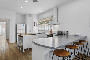 A modern kitchen with white cabinetry, a large island with stools, a built-in oven, and a stainless steel range hood.