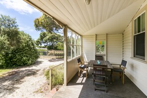 A covered patio with a table and chairs, a view of the surrounding greenery, and a window with a view of the trees.