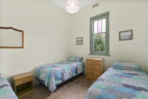 Un dormitorio con dos camas individuales, un aparador, una mesita de noche de madera, una ventana con vistas a zonas verdes y una lámpara colgante.