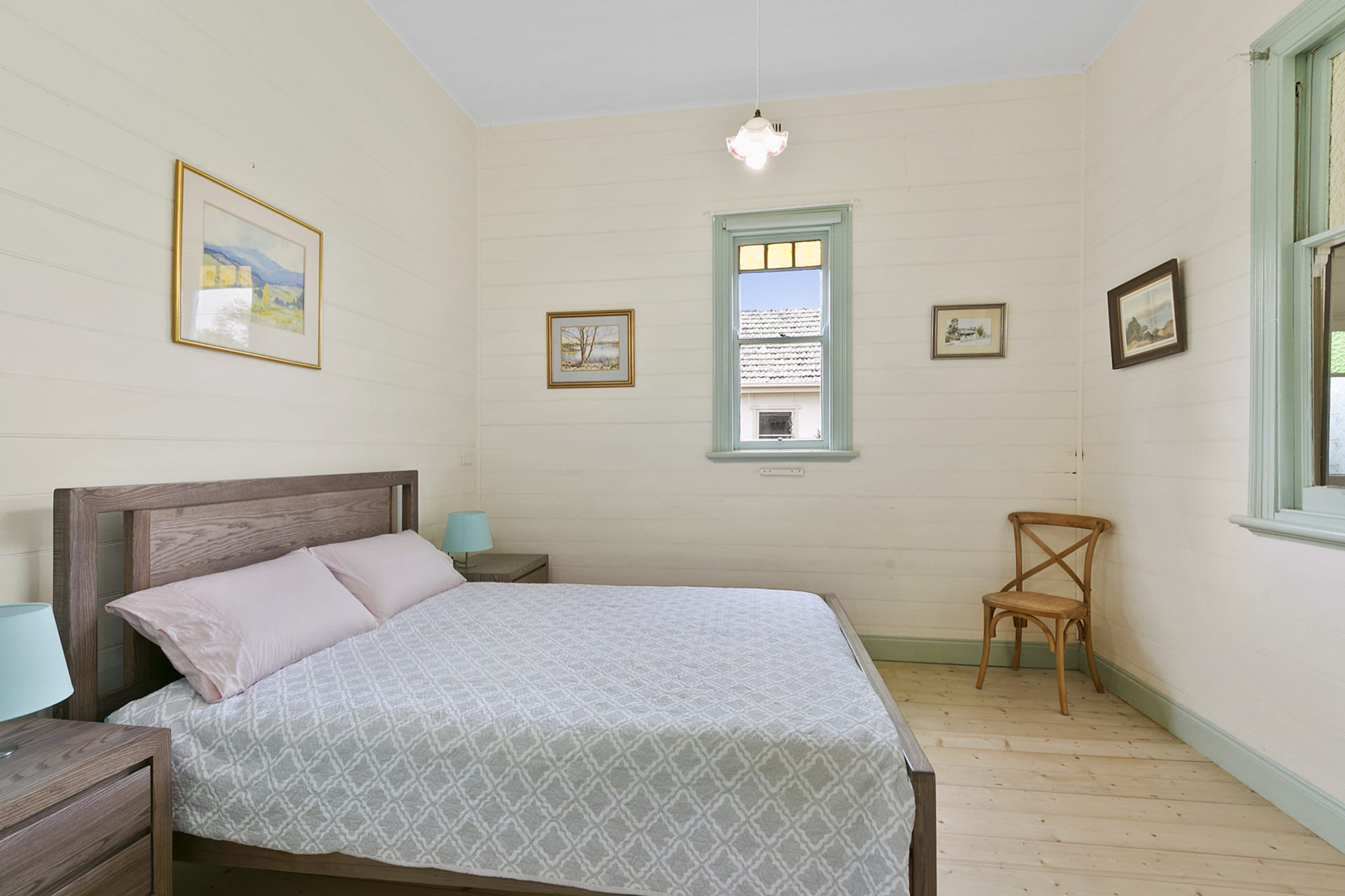 Quarto com cama, cadeira, mesa de cabeceira, abajur e janela.