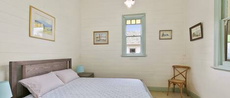 Quarto com cama, cadeira, mesa de cabeceira, abajur e janela.