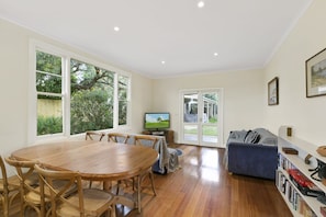 A spacious living area with a wooden dining table, a blue sofa, and a television.