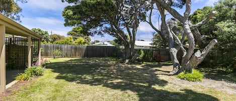 A backyard with a wooden fence, a tree, and a building with a sloped roof.