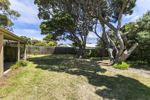 A backyard with a wooden fence, a tree, and a building with a sloped roof.