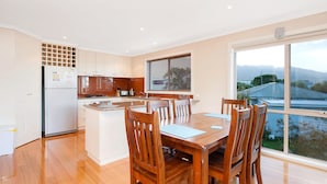 A modern kitchen with a dining area, wooden chairs, a large window, and a view of the outdoors.