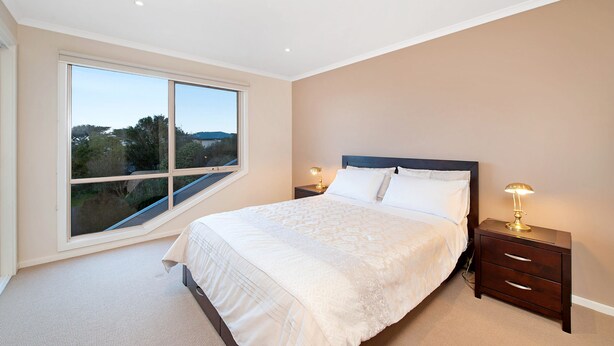 A bedroom with a large window, a bed with white linens, two bedside tables with lamps, and a view of the outdoors.