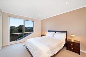 A bedroom with a large window, a bed with white linens, two bedside tables with lamps, and a view of the outdoors.