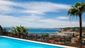 Une piscine d’un bleu éclatant, avec vue sur la mer et les bâtiments.