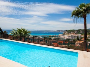 Une piscine d’un bleu éclatant, avec vue sur la mer et les bâtiments.