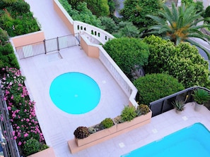 A rooftop pool with a circular design, surrounded by lush greenery and a white railing.