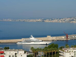 Eine große Yacht liegt in einer Marina vor einer Stadtlandschaft.