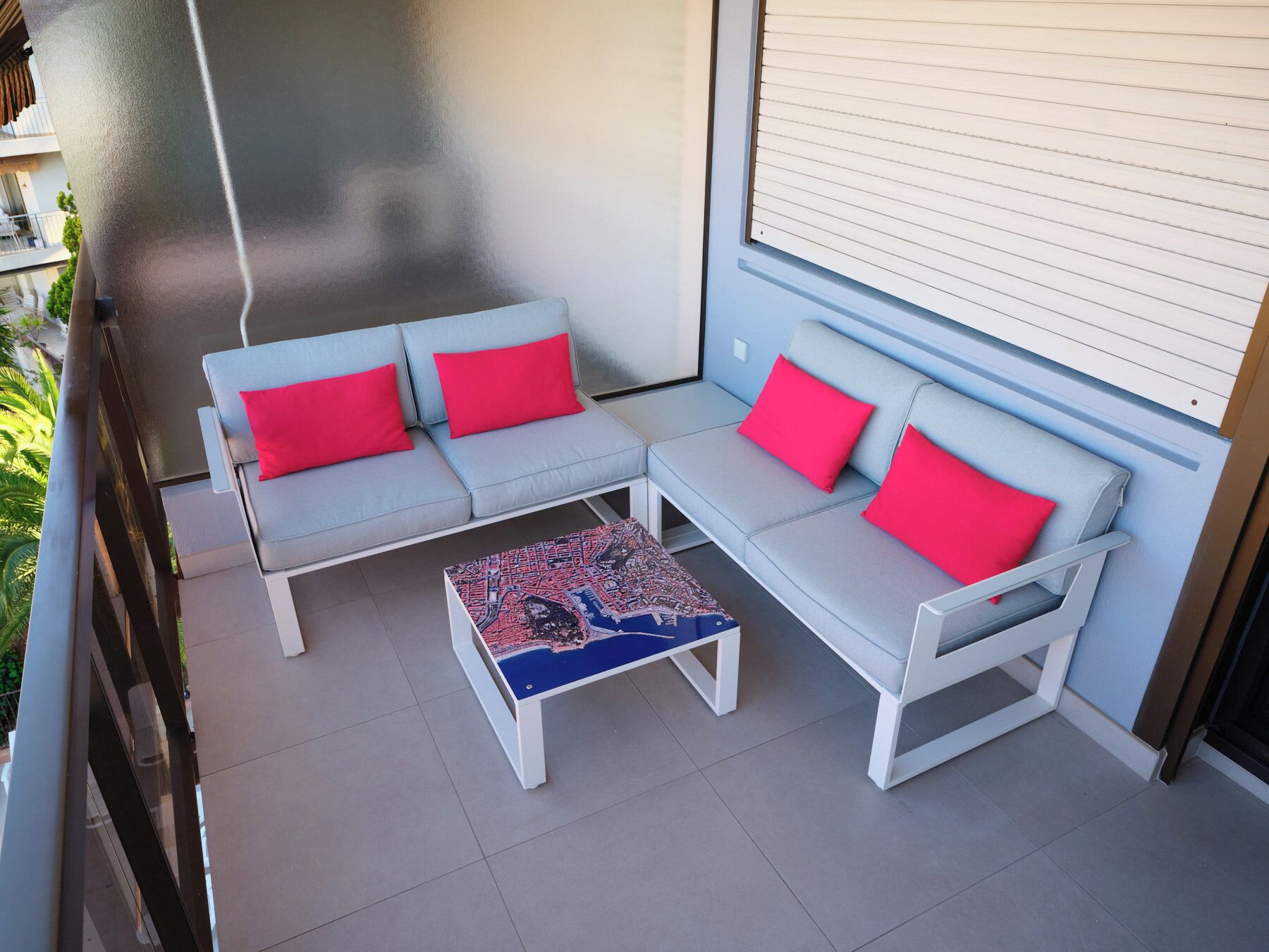 Un balcon agrémenté d’un ensemble de meubles de jardin blancs, de coussins rouges et d’une table basse à motifs.