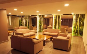 Un vestíbulo en la planta baja con sofás color beige, una mesa de centro de madera y un panel decorativo de bambú.