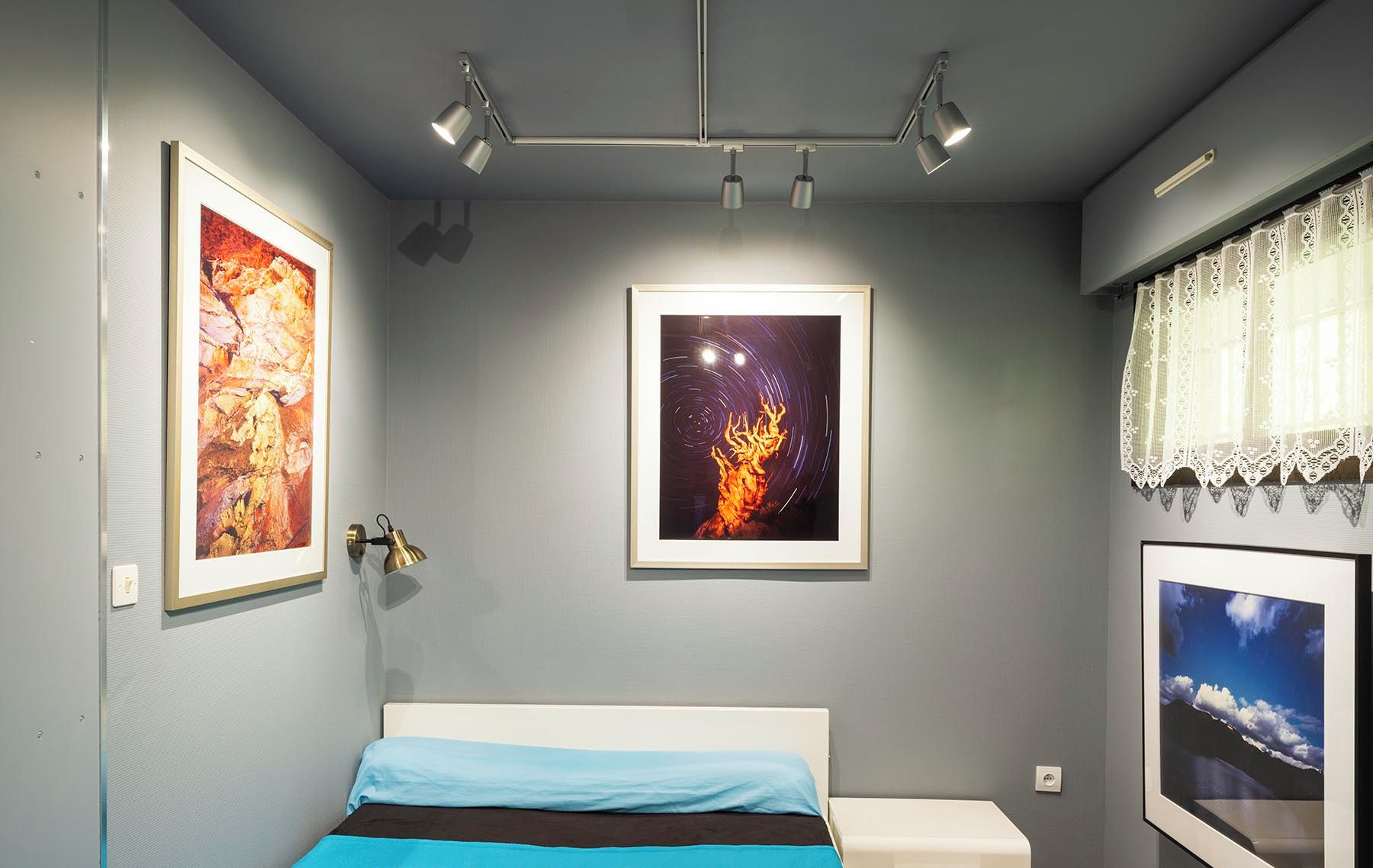 Un dormitorio con cama de 140x190 cm, cuadros de arte y vistas al cielo nocturno.