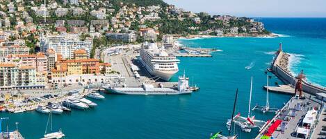 A coastal cityscape with a marina, apartment buildings, and a large cruise ship docked at the port.