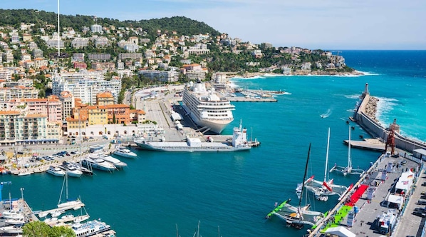 Un paisaje urbano costero con un puerto deportivo, edificios de apartamentos y un gran crucero atracado en el puerto.