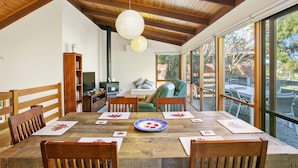 A dining area with a wooden table, chairs, and a view of the outdoors through large windows. - Apollo Bay People N Paws (Apollo Bay)