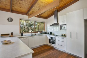 A modern kitchen with white cabinets, a stainless steel range, and a large window. - Apollo Bay People N Paws (Apollo Bay)