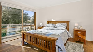 A bedroom with a large window, wooden bed, bedside tables, and a rug. - Apollo Bay People N Paws (Apollo Bay)