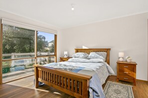 Ein Schlafzimmer mit einem großen Fenster, einem hölzernen Bett, Nachttischen und einem Teppich.