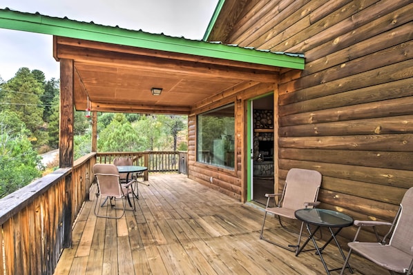 A wooden deck with a covered area, outdoor seating, and a view of the surrounding forest.