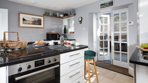 A modern kitchen with a black countertop, white cabinets, and a dining area with a green chair. - High House (6), Tenby , Pembrokeshire (Tenby)