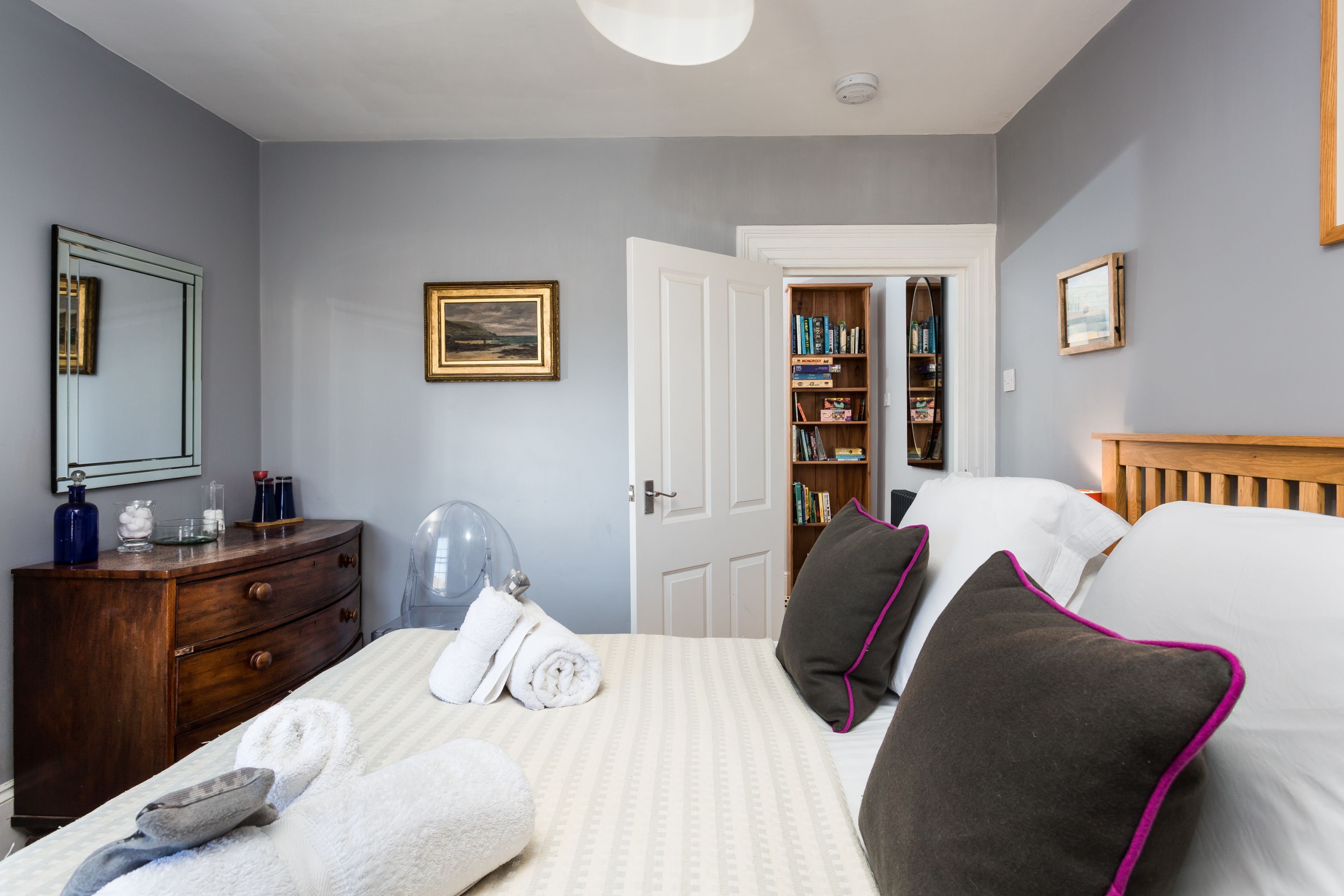 A bedroom with a bed, a dresser, a bookshelf, and a door leading to another room.