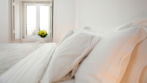 A bedroom with a large bed, a window with a view, and a vase with flowers. - Arthistorian's Residence ★ central & sunny (Lisboa)