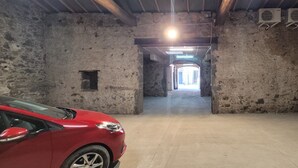 Un'auto parcheggiata in un corridoio stretto, delimitato da pareti in pietra e con pavimento in cemento, che conduce verso una zona più luminosa con luce naturale.