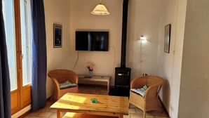 Un accogliente soggiorno con un tavolo in legno, due poltrone in vimini, una televisione, un camino e un quadro appeso al muro.