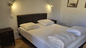 Un letto rifatto con lenzuola e cuscini bianchi, una testiera scura e un comodino con una lampada.