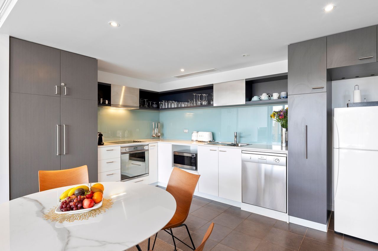 A modern kitchen with grey cabinets, white countertops, and stainless steel appliances.
